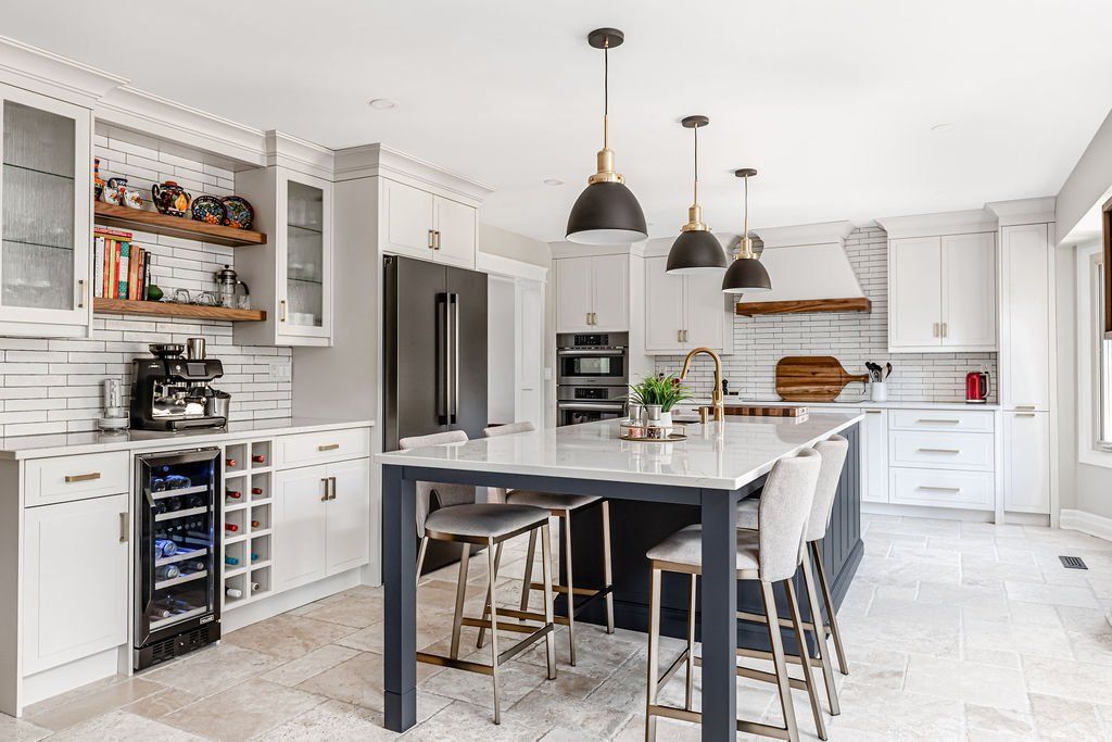 A kitchen with white cabinets , a large island , stools and a refrigerator.
