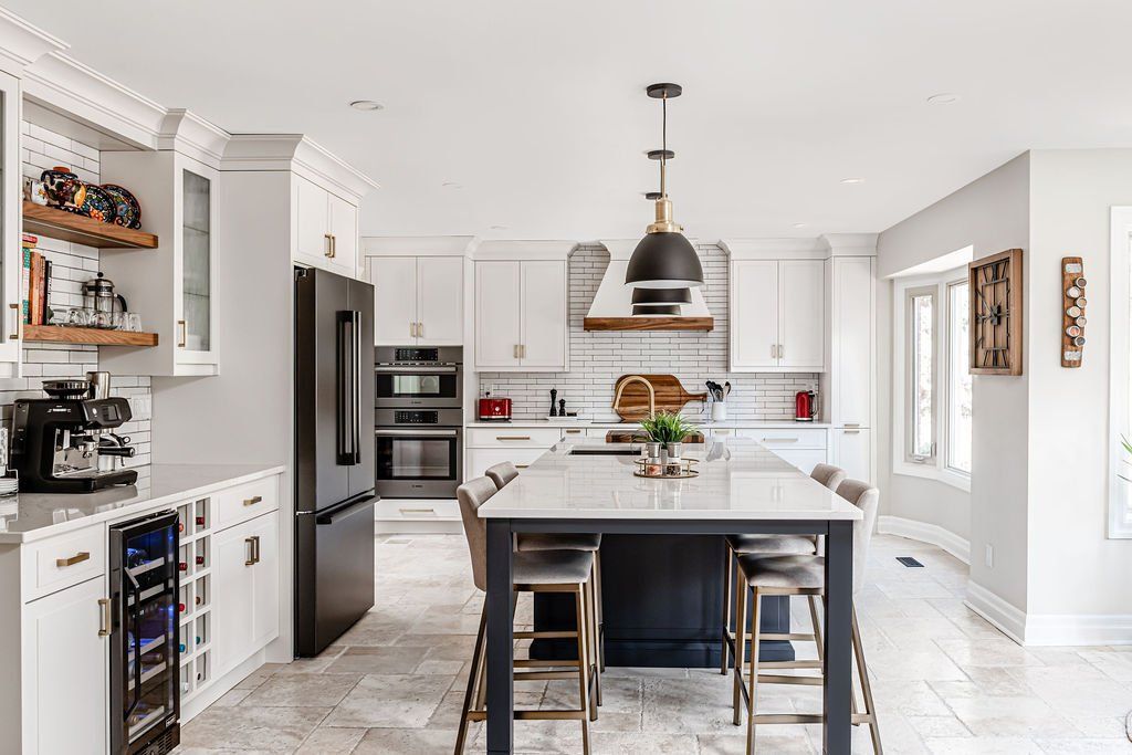 A kitchen with white cabinets , black appliances , a large island and stools.