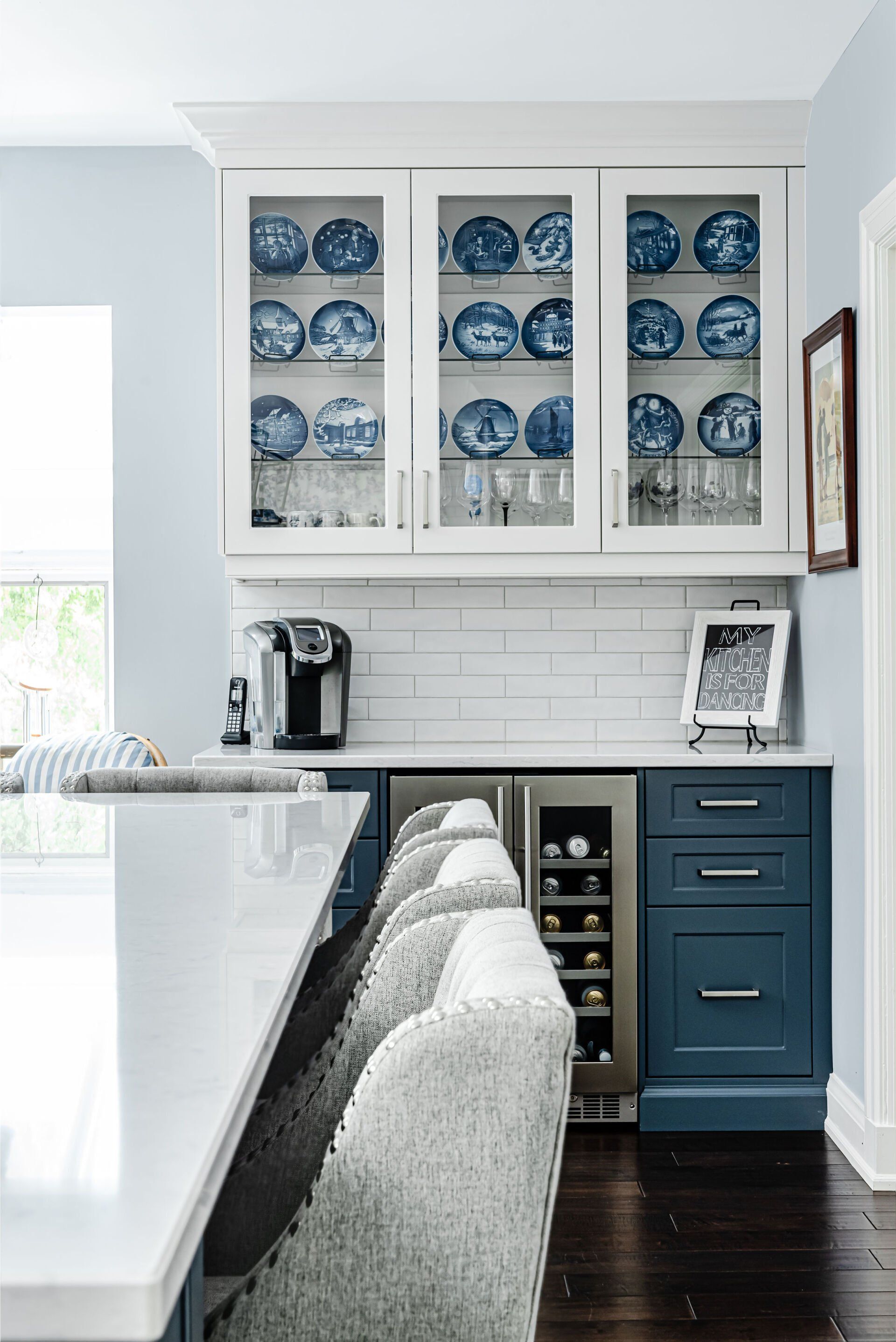 A kitchen with blue cabinets , white counter tops , and a wine cooler.