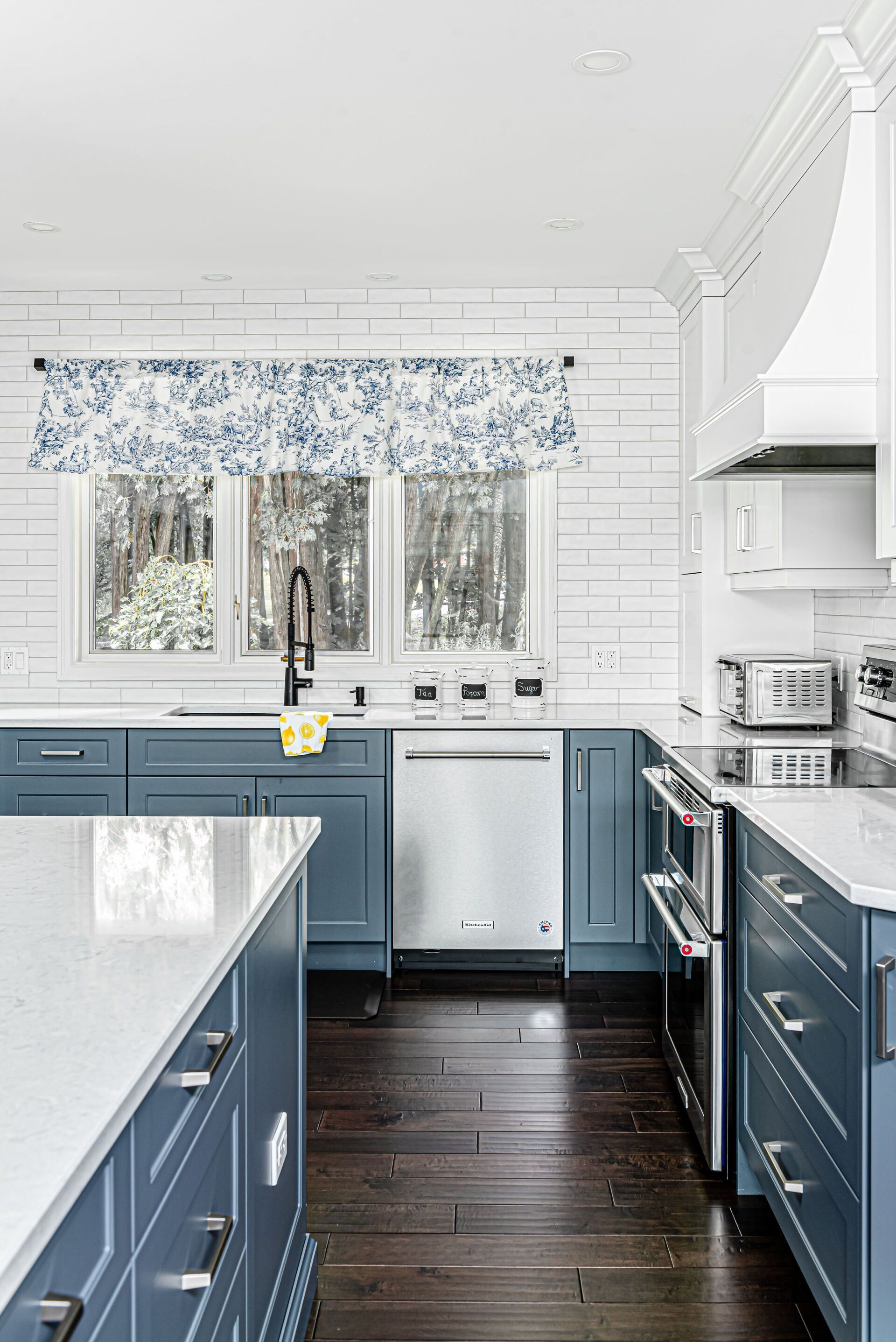 A kitchen with blue cabinets , white counter tops , and stainless steel appliances.