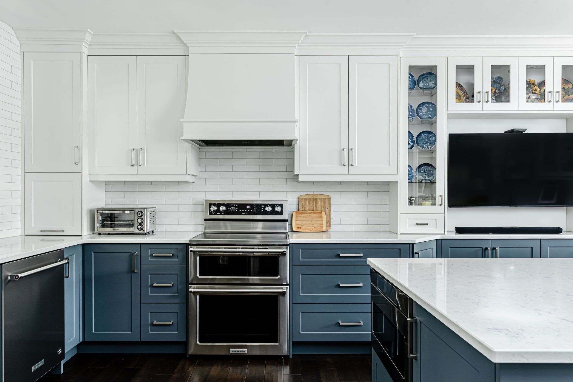 A kitchen with blue cabinets , white cabinets , stainless steel appliances and a flat screen tv.