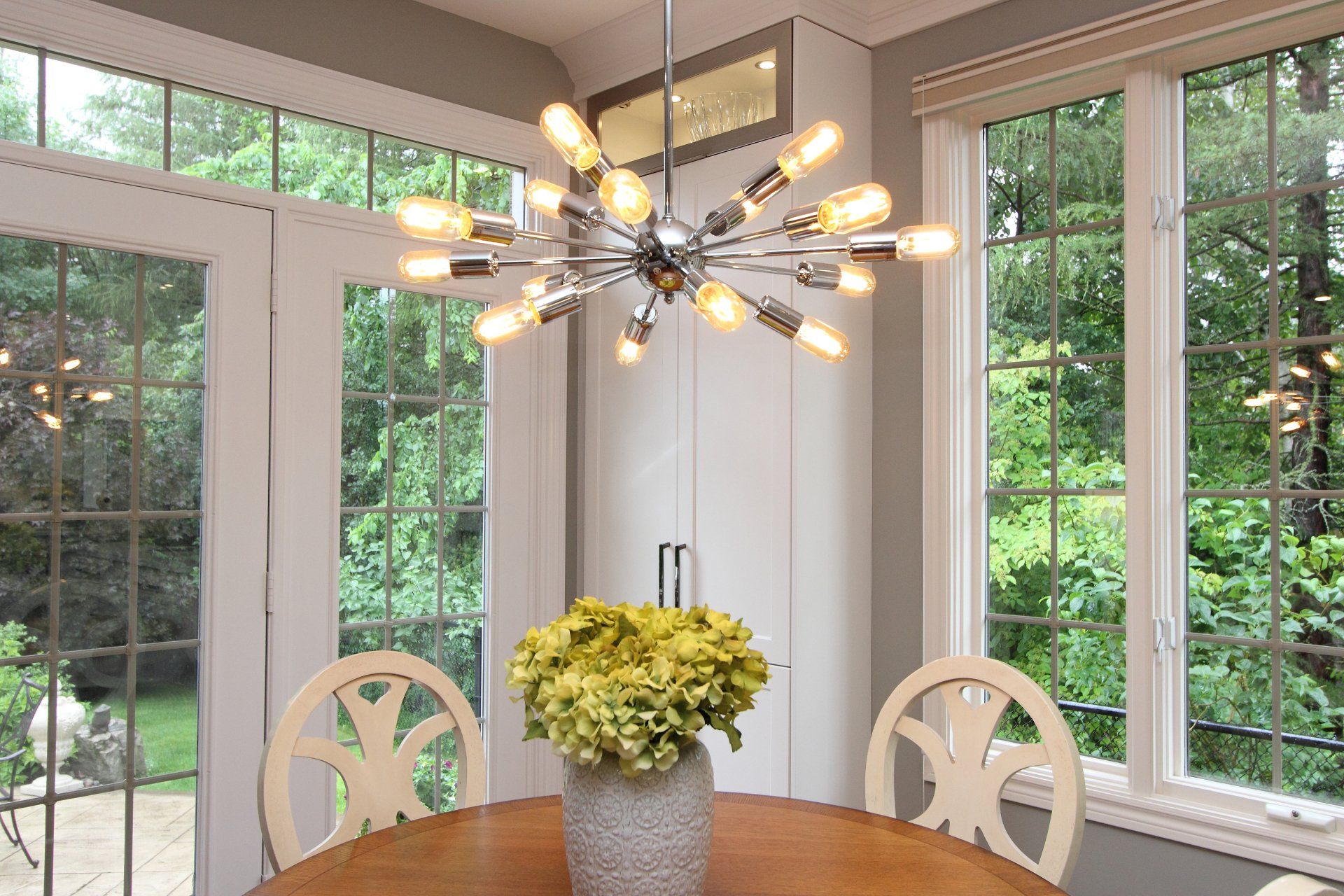 A dining room table with a vase of flowers on it and a chandelier hanging from the ceiling.