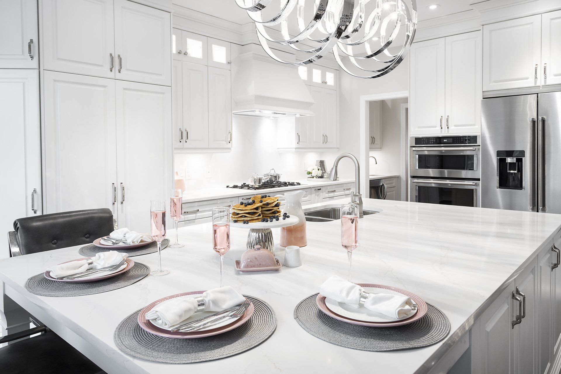 A kitchen with white cabinets , stainless steel appliances , and a large island with plates and glasses on it.