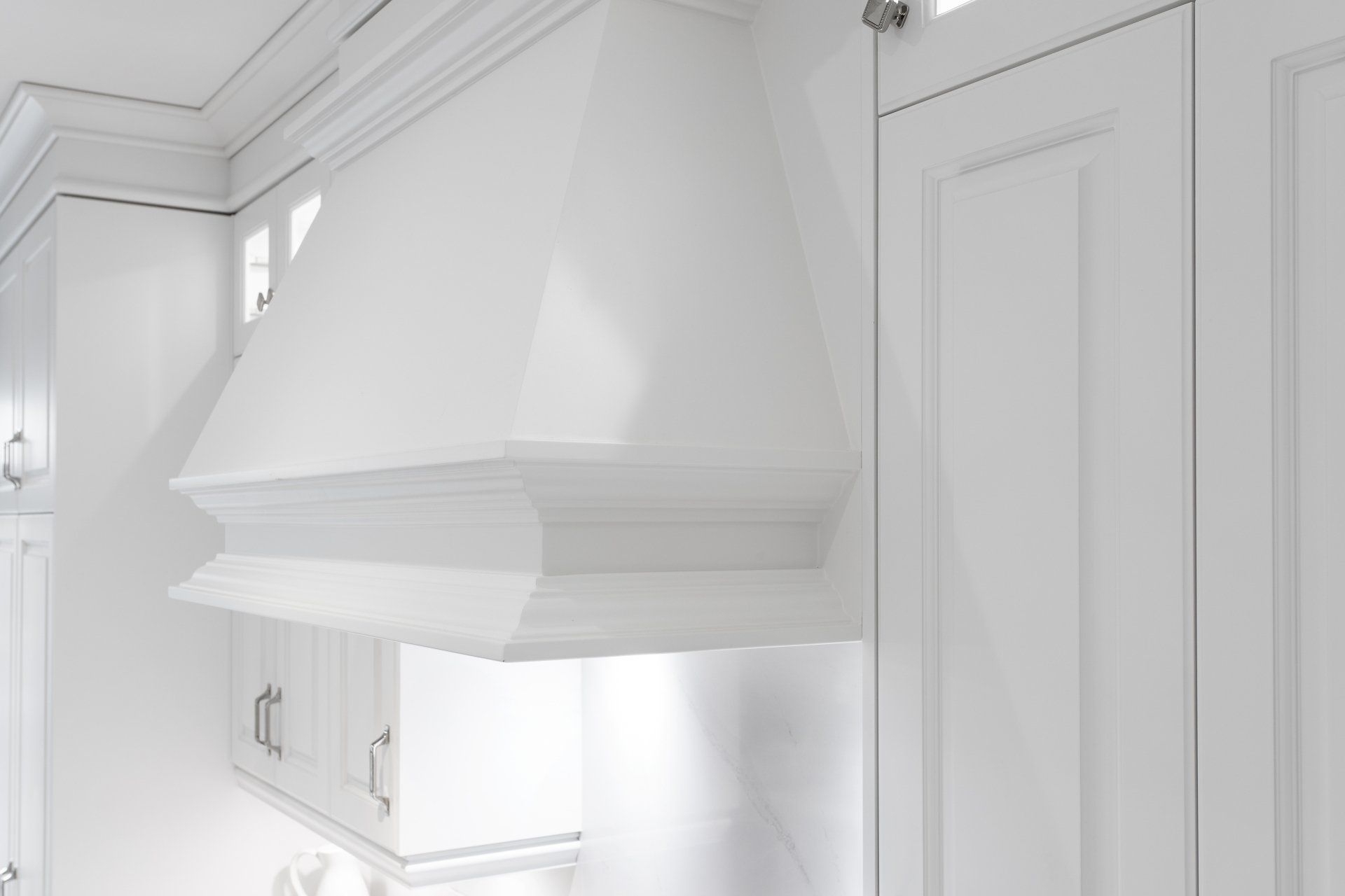 A kitchen with white cabinets and a hood above the stove.