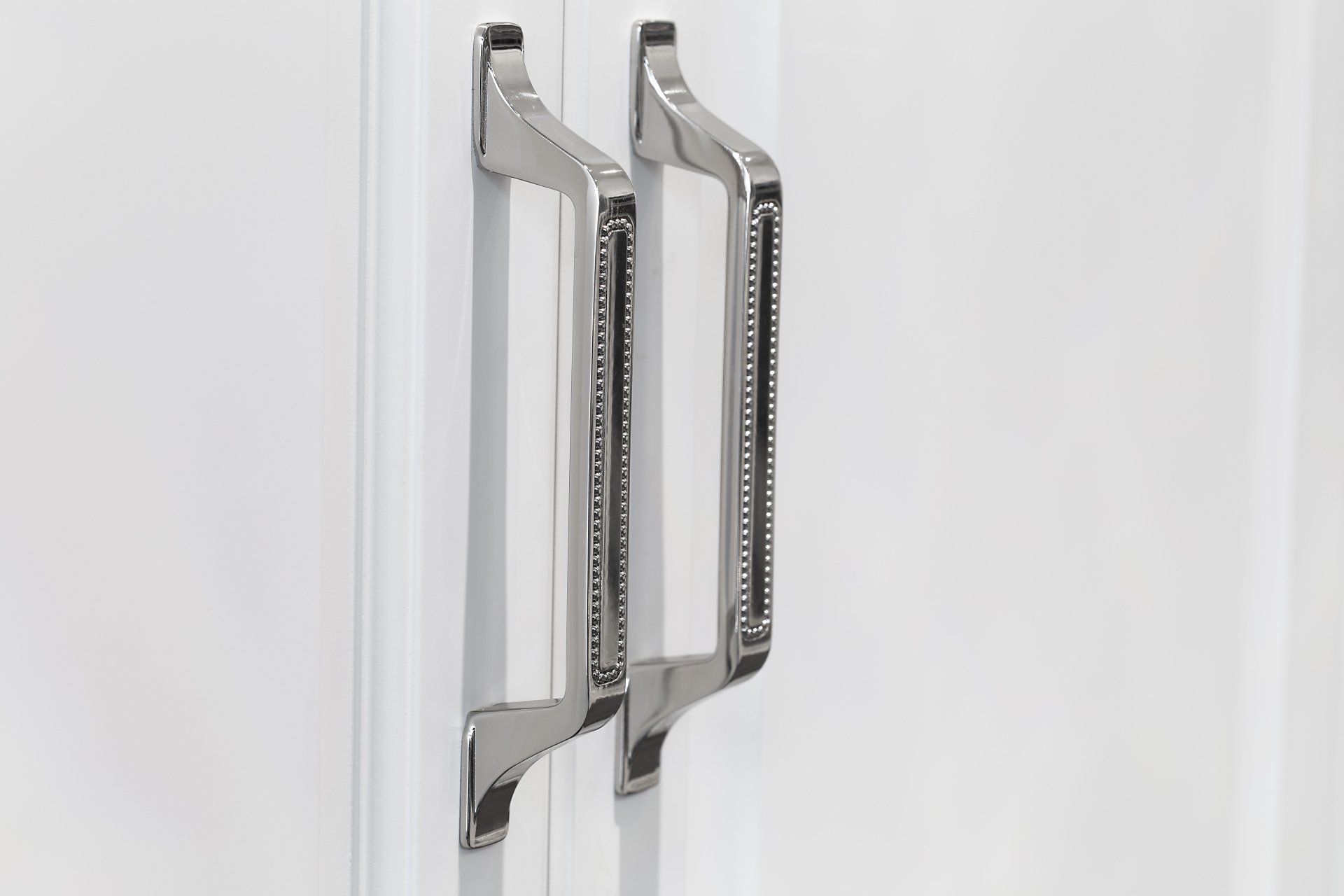 A pair of chrome cabinet handles on a white cabinet.