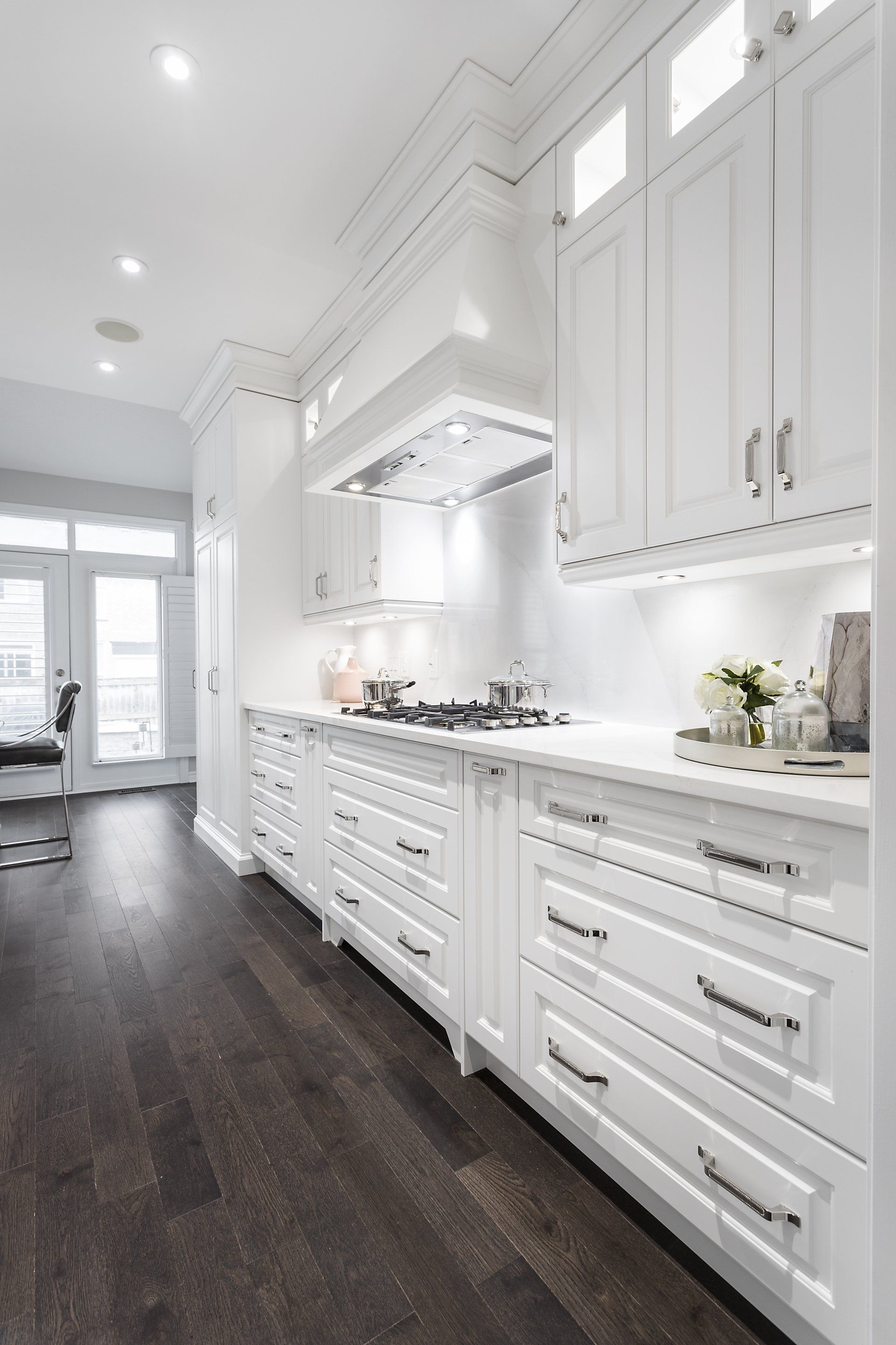 A kitchen with white cabinets and dark wood floors.