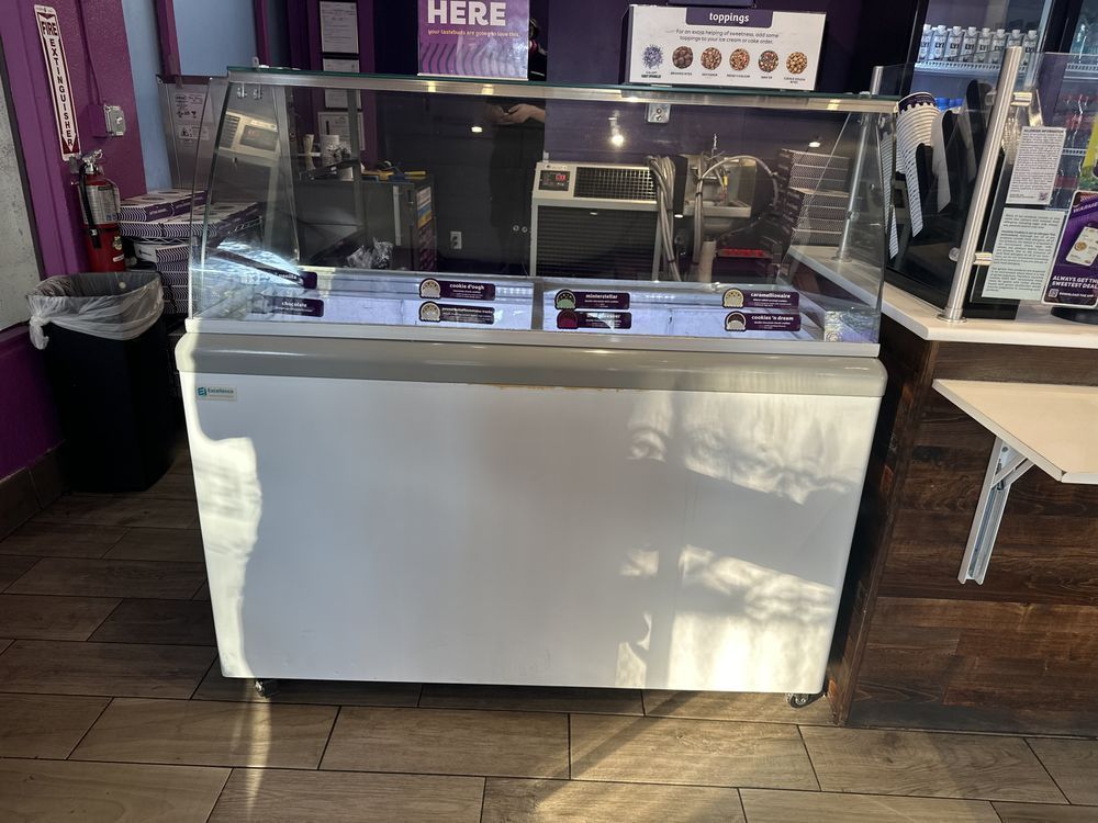 Empty café display case with glass shelves and white base under purple lighting