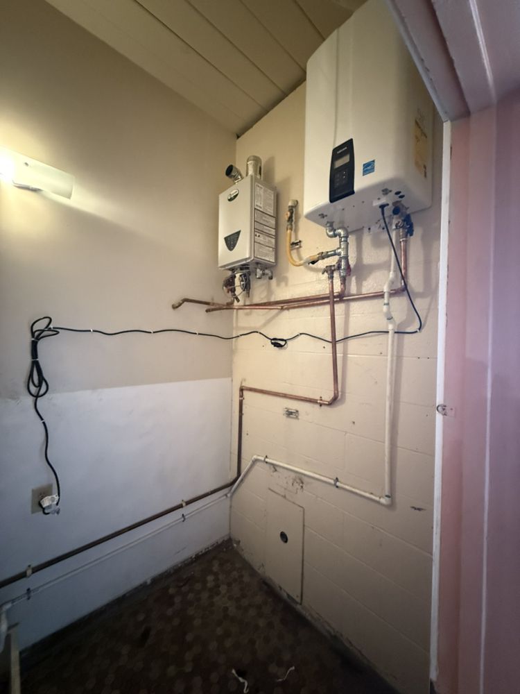 Indoor utility wall with electrical boxes, exposed wiring, and pipes in a narrow room.