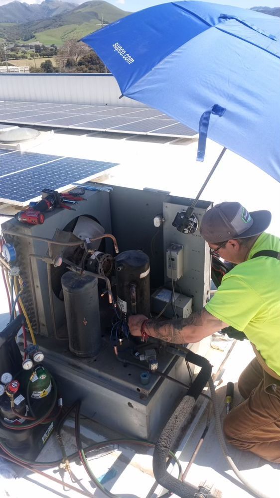 Technician repairing rooftop HVAC unit under a blue umbrella on a sunny day