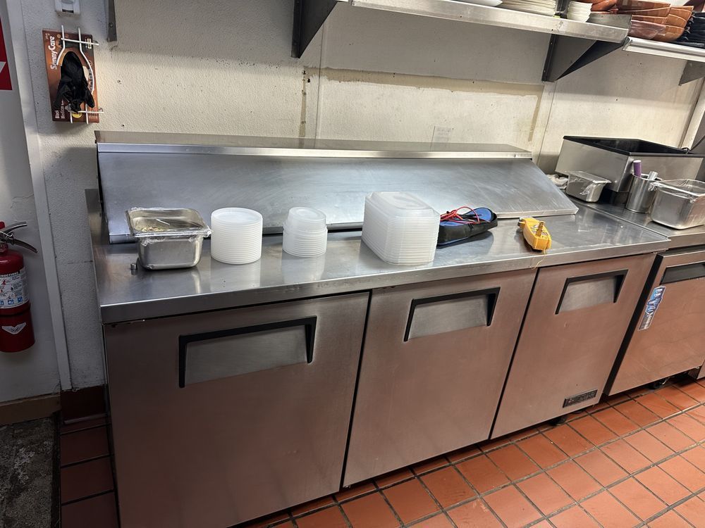 Commercial kitchen prep counter with stacked white bowls and a few utensils on a stainless steel surface.
