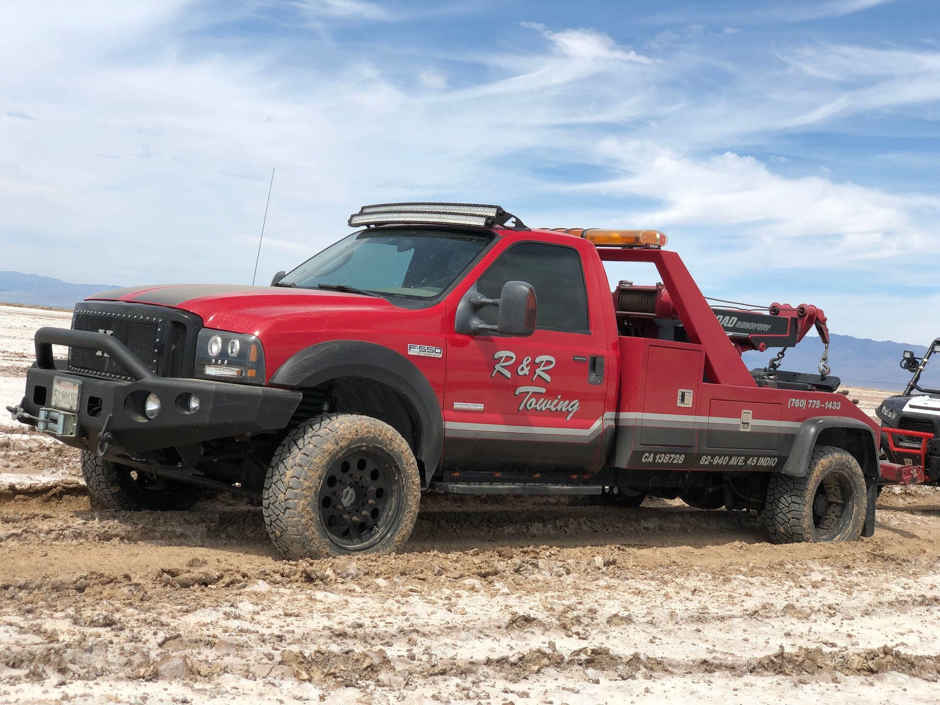A red tow truck is parked in the middle of a dirt field.