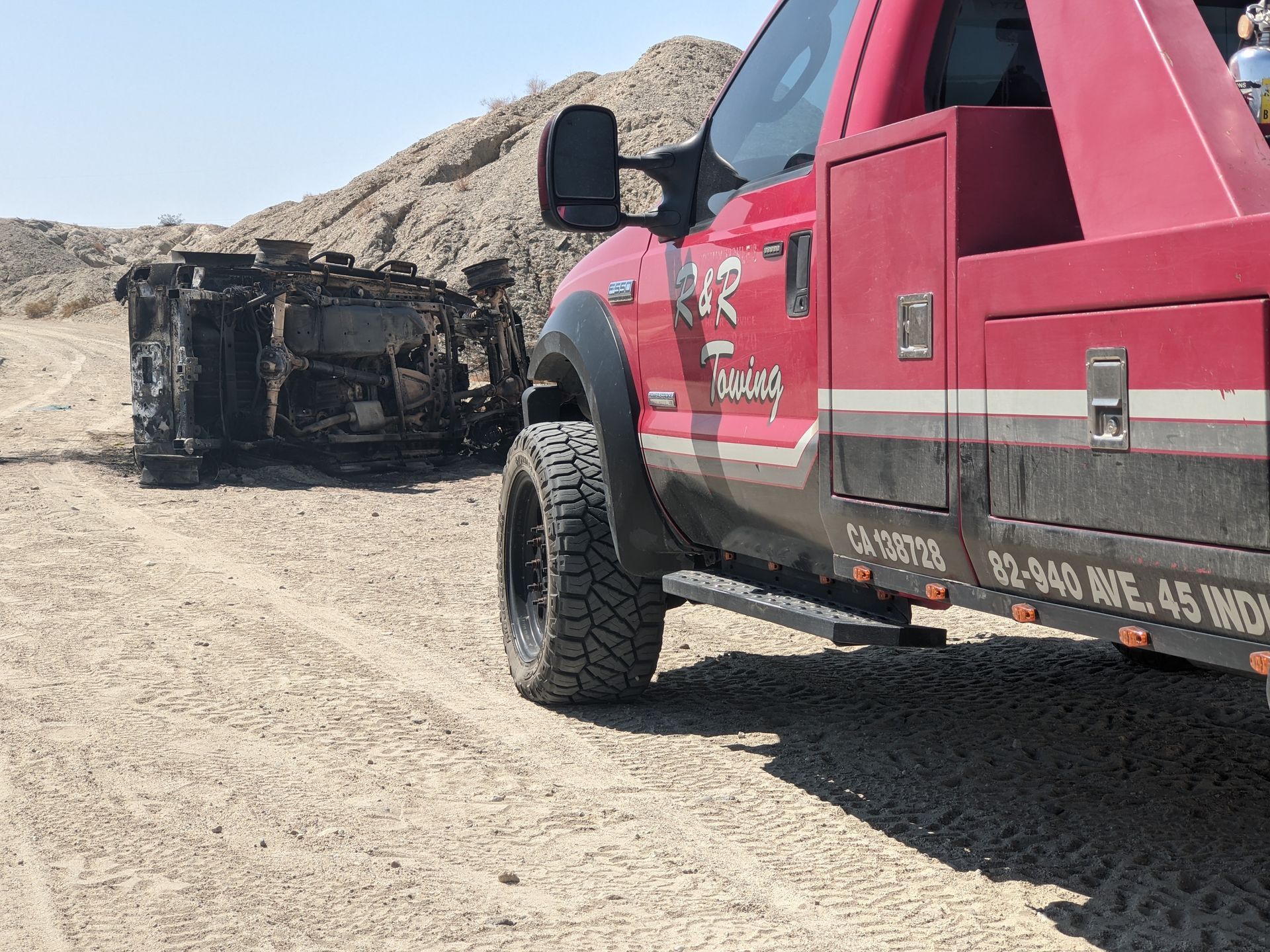A red tow truck is towing a broken down vehicle in the desert.