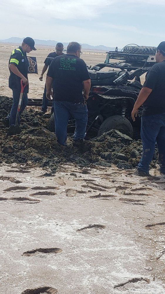 A group of men are standing around a vehicle in the mud.