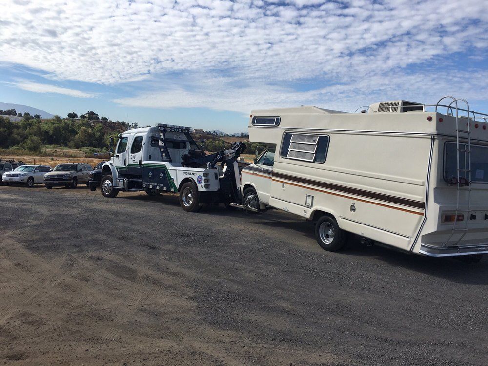 A rv is being towed by a tow truck in a parking lot.