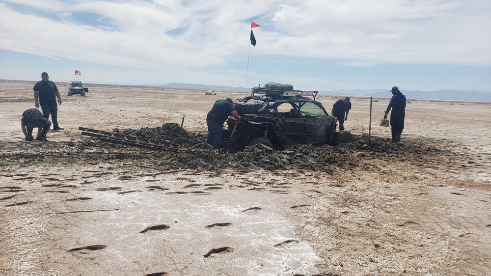 A group of people are working on a vehicle that is stuck in the mud.