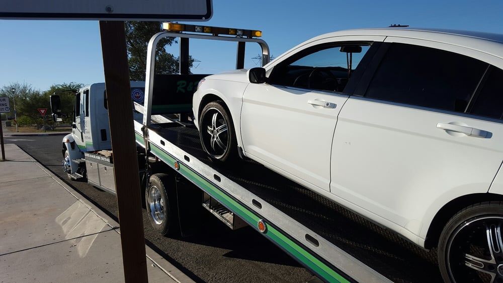 A white car is being towed by a tow truck.