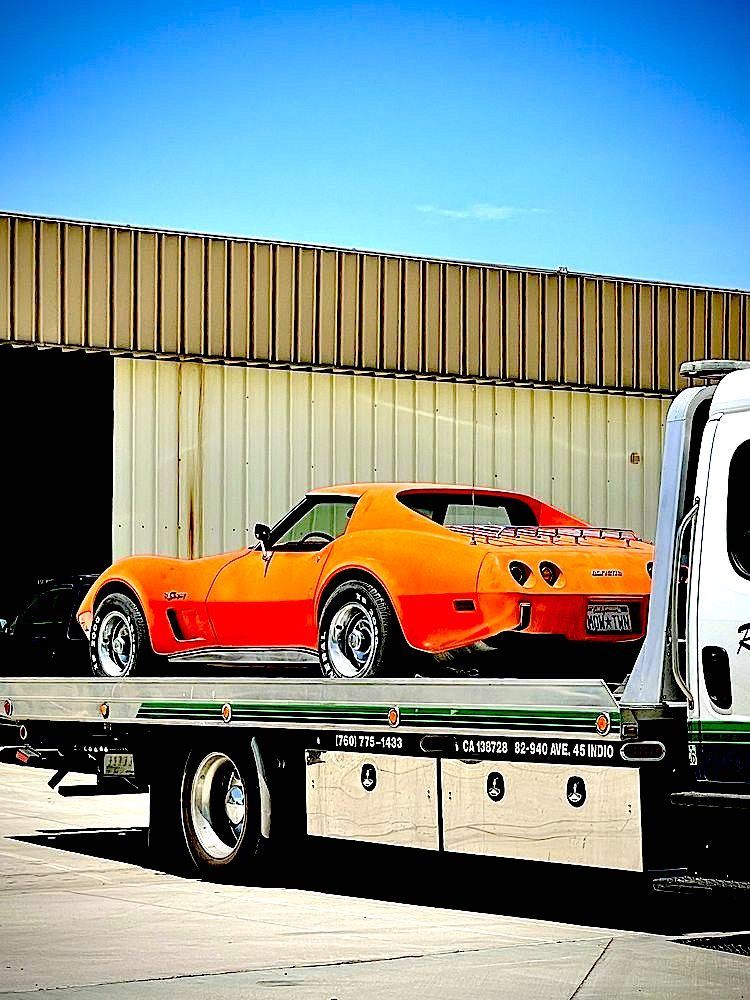 An orange corvette is being towed by a tow truck.