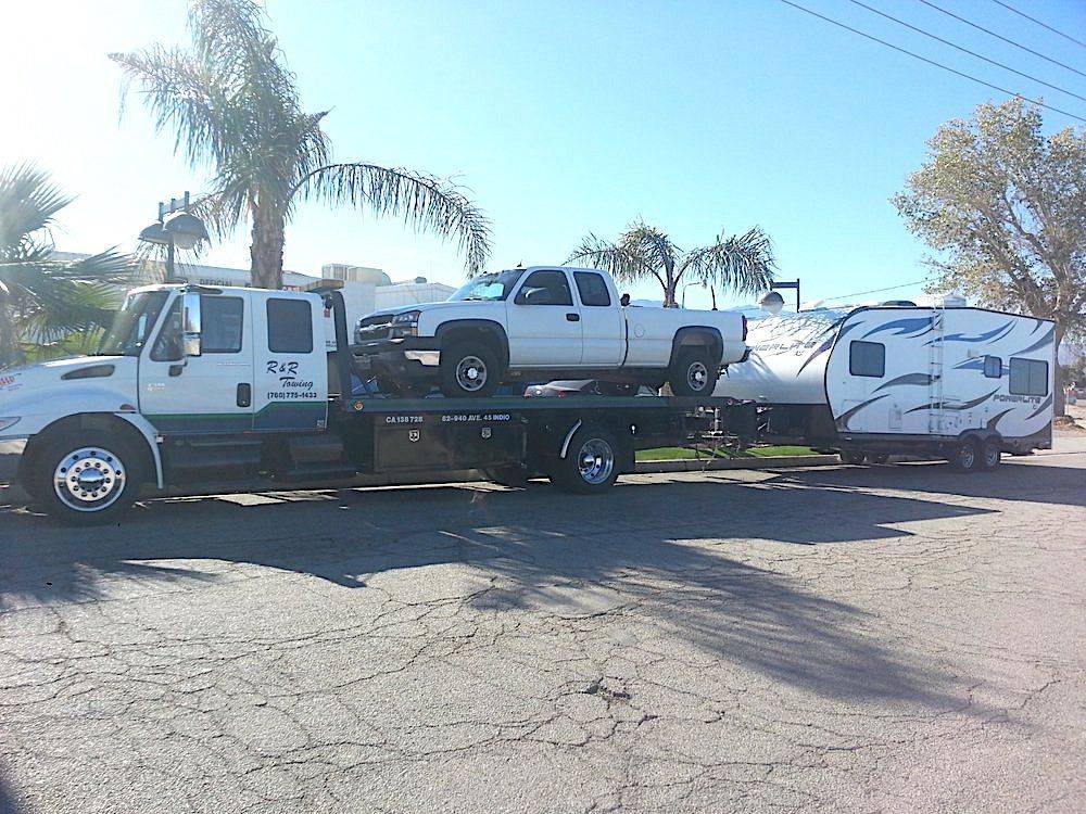 A tow truck is carrying a truck and a trailer