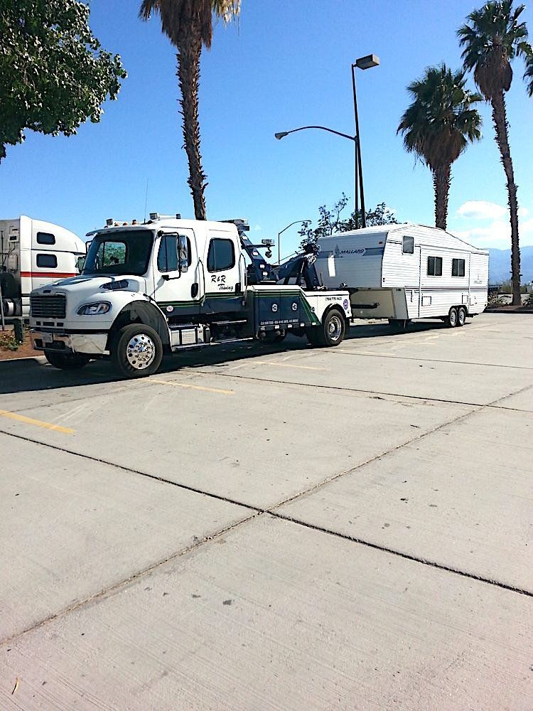 A tow truck is pulling a trailer in a parking lot