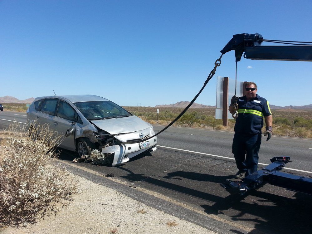 A man is standing next to a damaged car on the side of the road