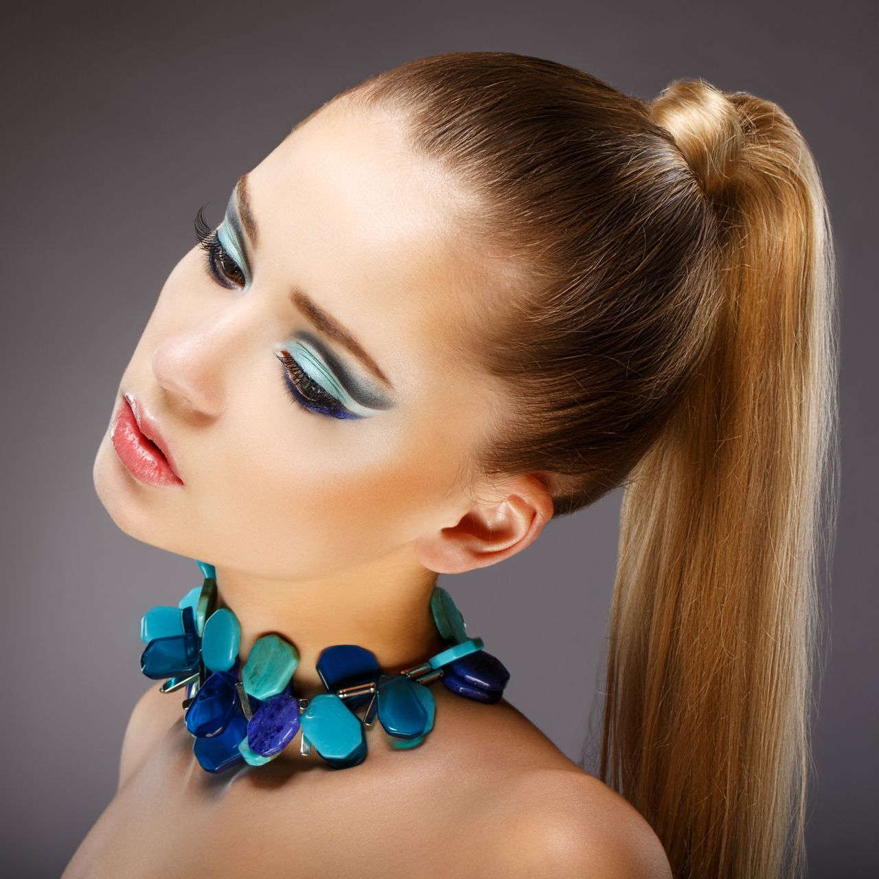 The woman is wearing a blue necklace and a ponytail.