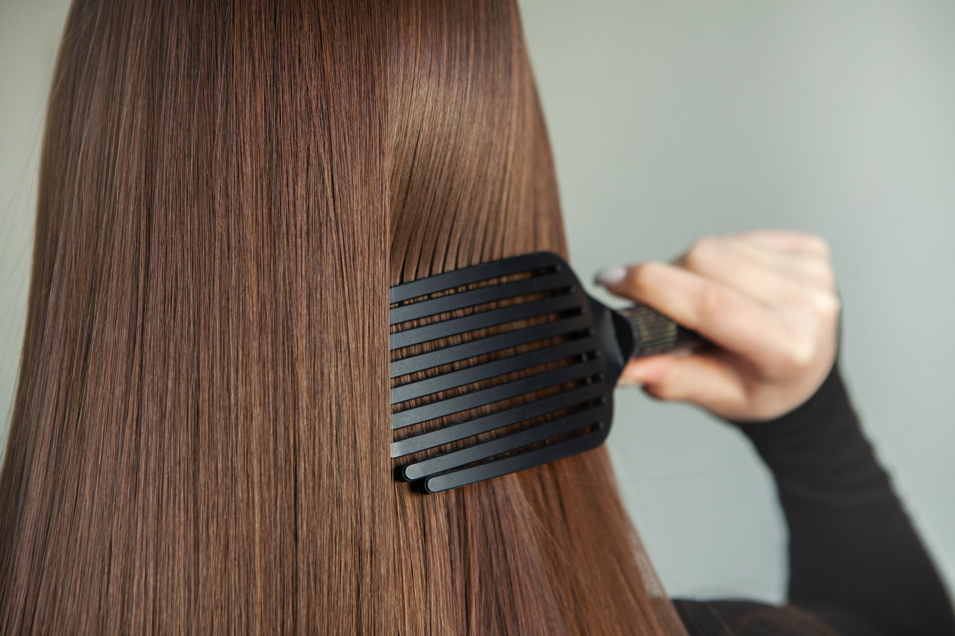 A woman is brushing her long brown hair with a black comb.