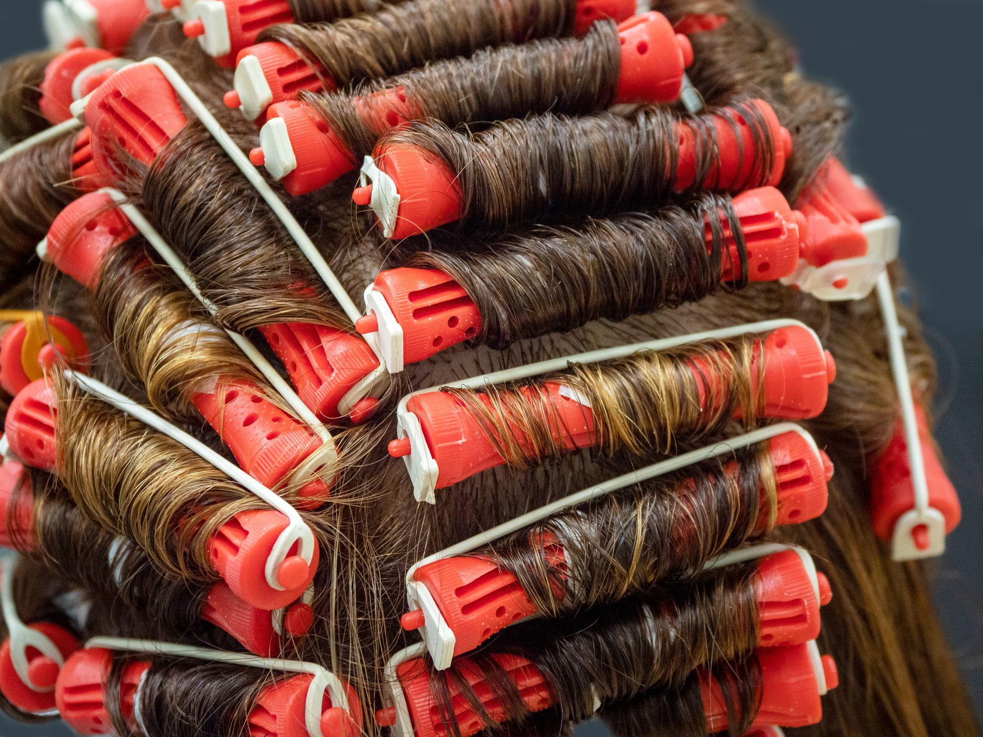 A woman is getting her hair curled with red and white rollers.