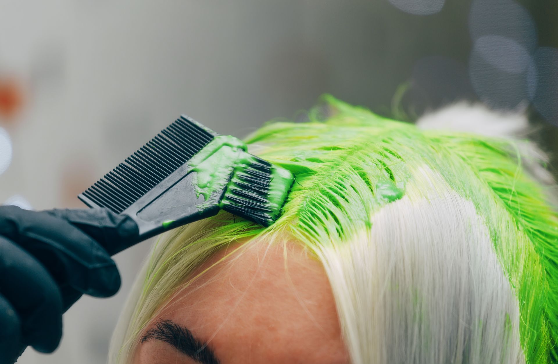A woman is getting her hair dyed green by a hairdresser.