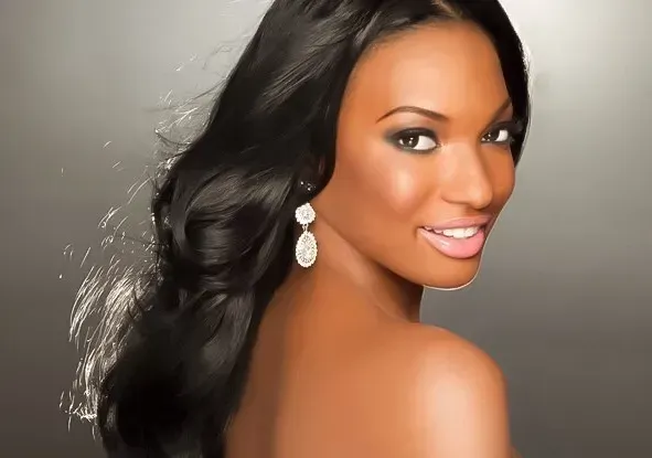 Smiling woman with long black hair and dangling earrings, posing against a gray background