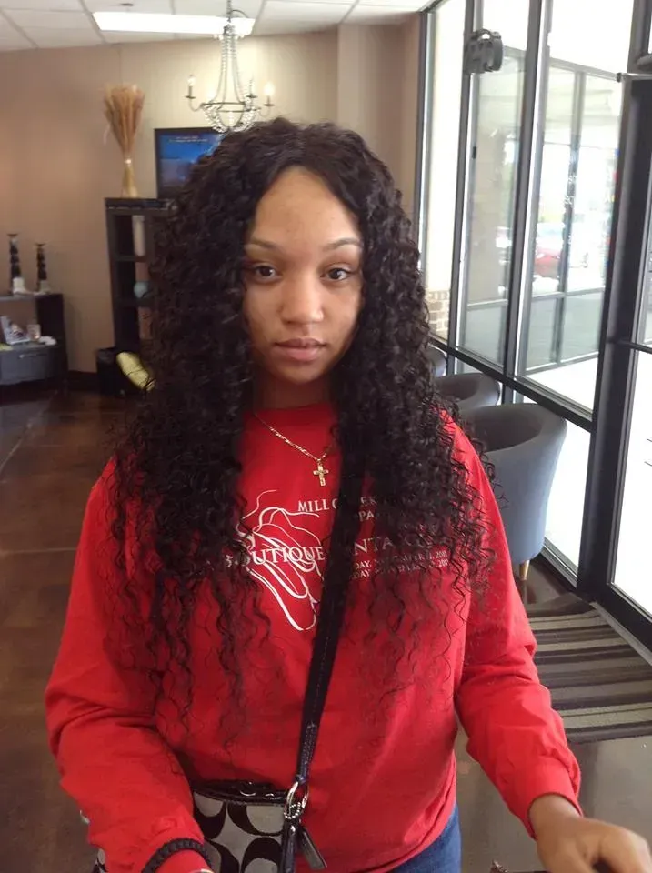 Person in a red sweatshirt and black crossbody bag standing indoors near large windows.
