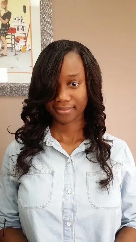 Woman in a light denim shirt smiling indoors against a beige wall.