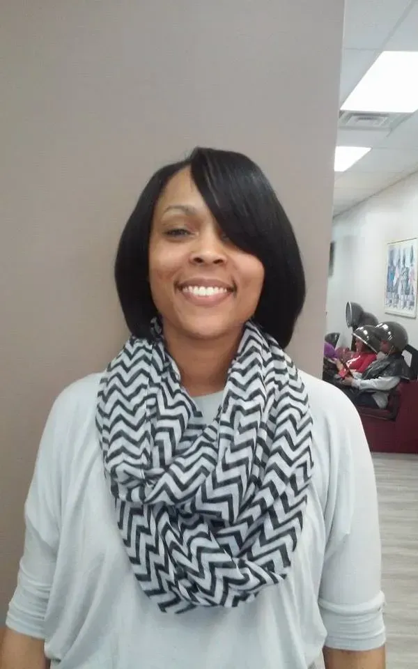 Smiling woman in a white top and black-and-white scarf standing in an office hallway