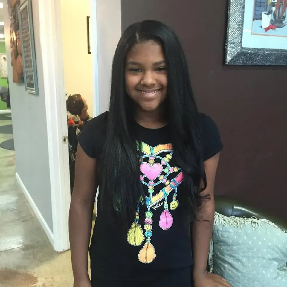 Smiling person in a black shirt with a colorful heart design standing indoors in a hallway