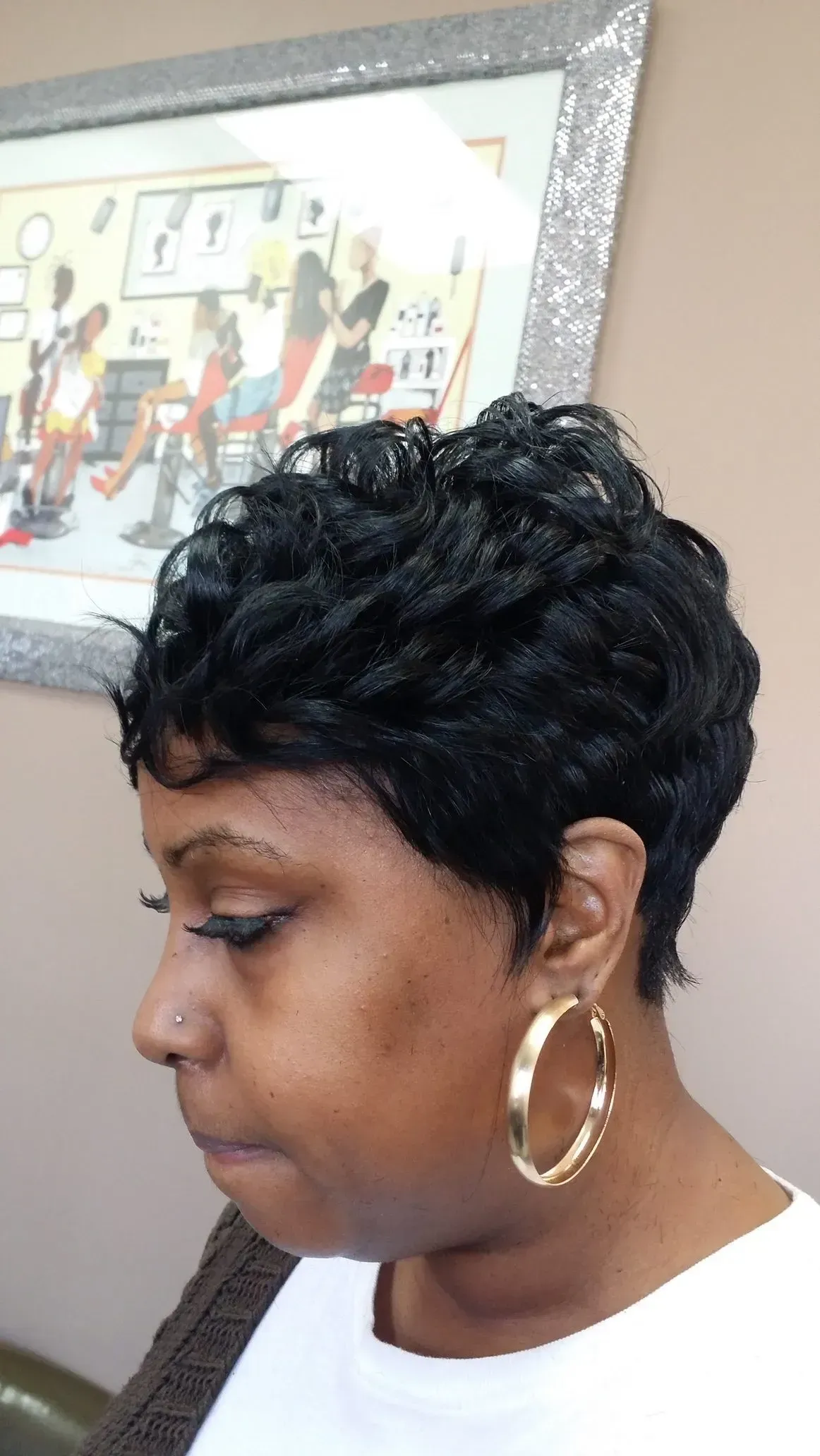 Side profile of a woman with short curly hair and gold hoop earrings, looking downward indoors.