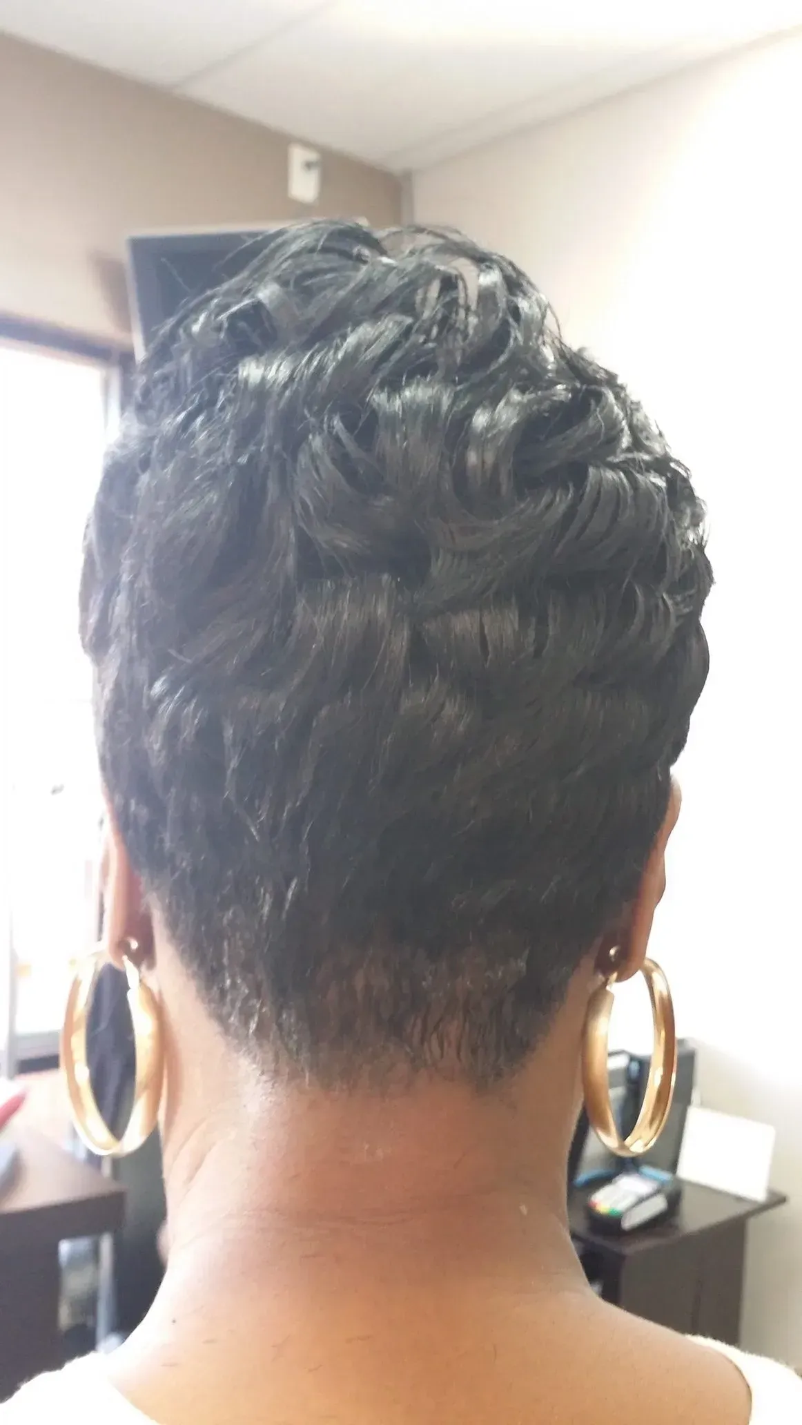 Back view of a short, styled updo with large hoop earrings in an indoor salon setting