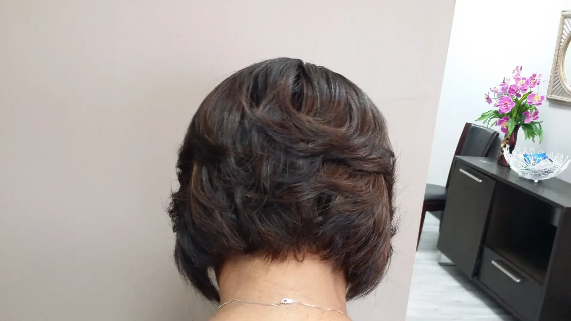 Back of a short dark-brown hairstyle with layered waves and a visible hair clip.