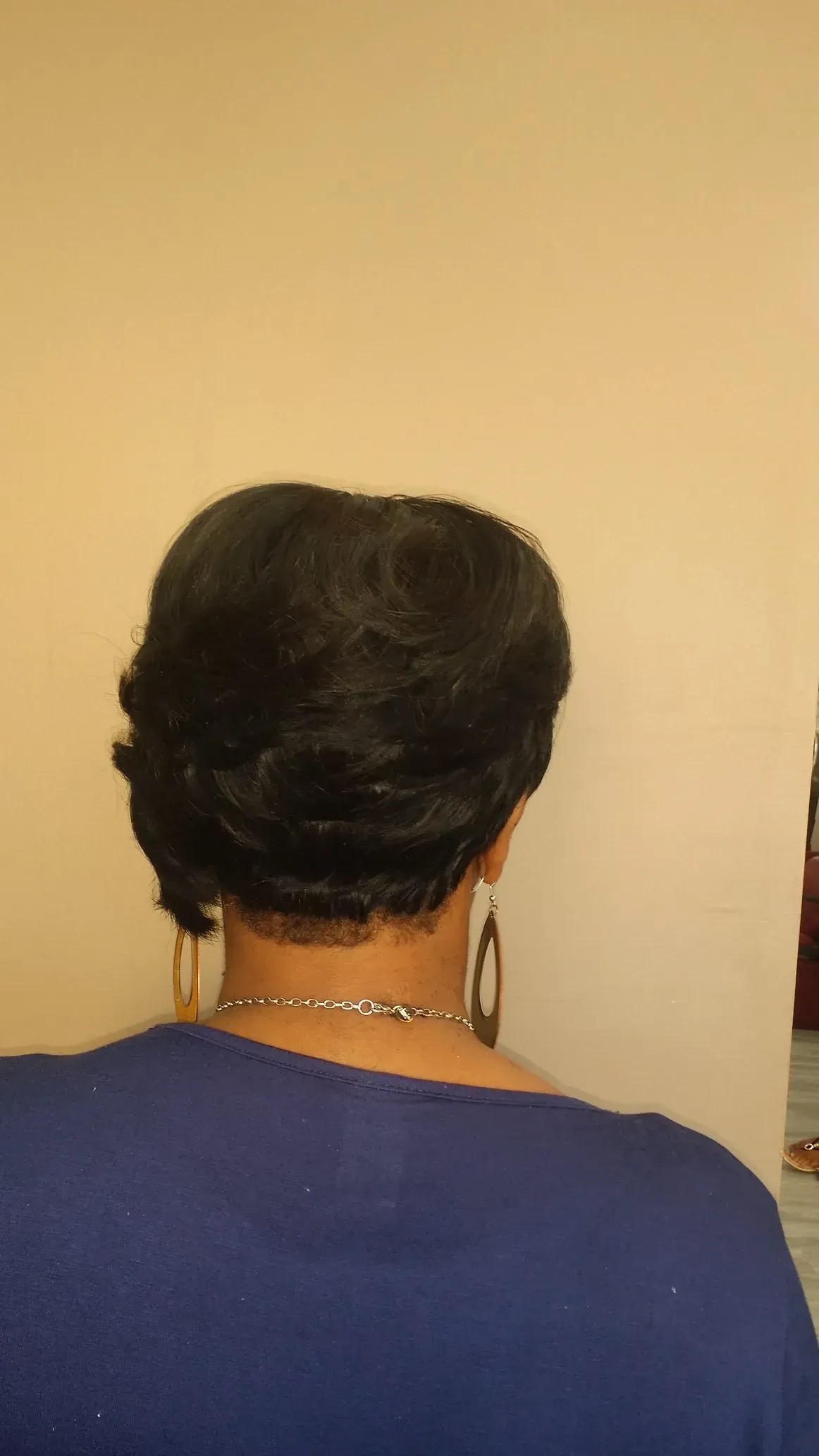Back of a person with short dark hair wearing a blue shirt, facing a beige wall.
