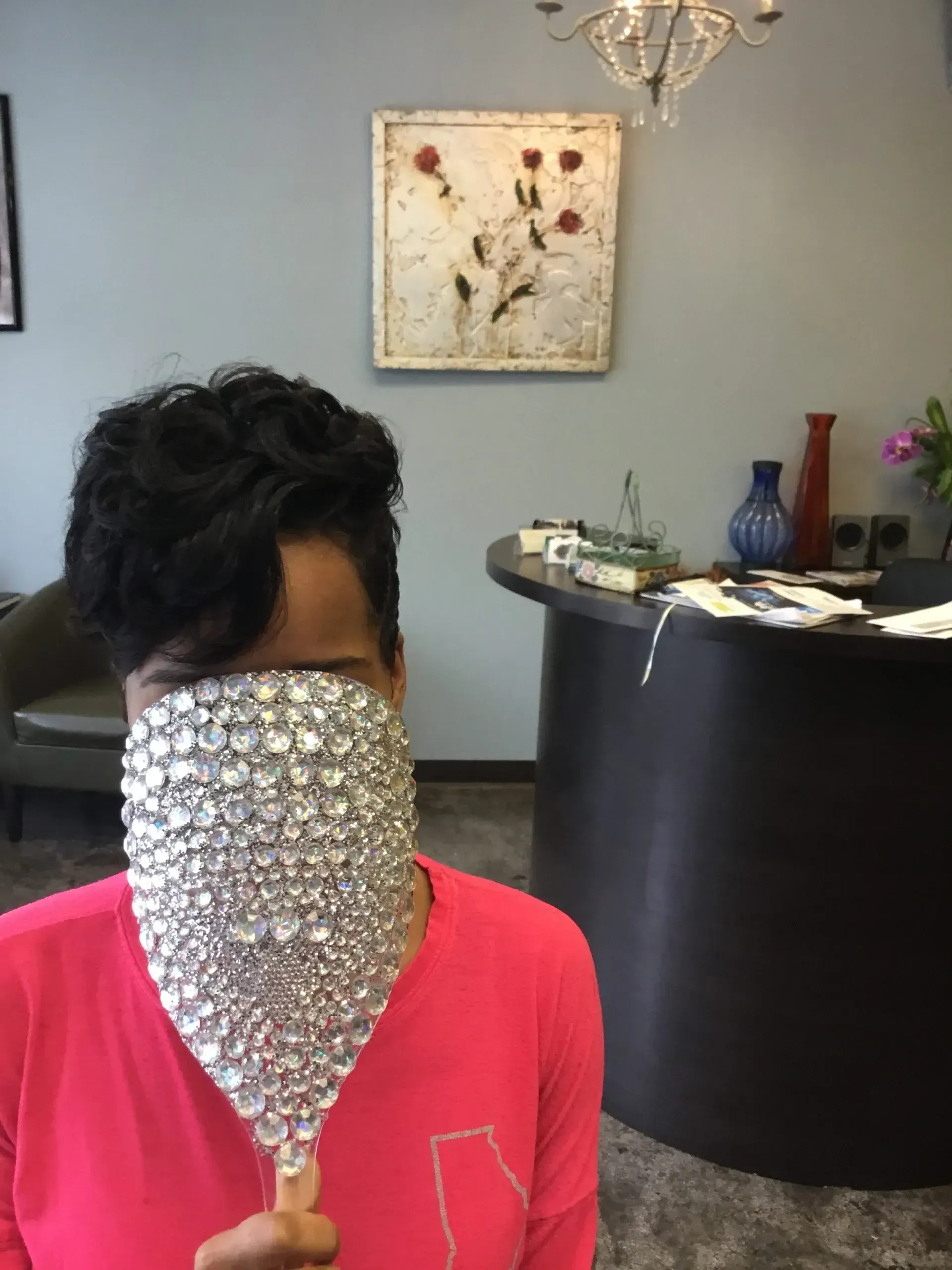 Person indoors with a sparkling silver face covering and red shirt, standing near a reception desk.