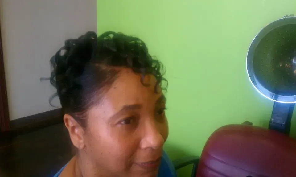 Person with curly hair indoors beside a green wall and round mirror, looking to the side.