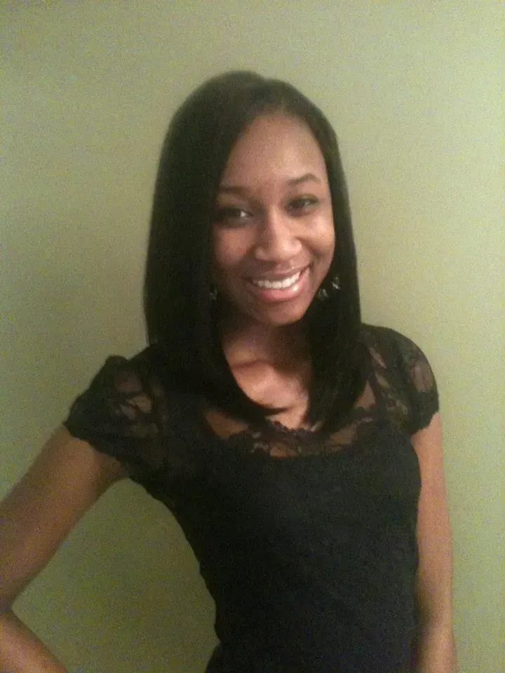 Smiling woman in a black top posing against a plain wall.