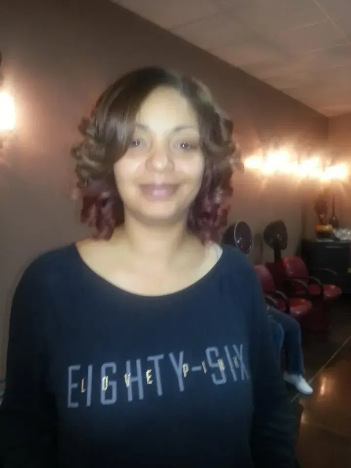 Woman standing indoors in a dim room, wearing a navy shirt with “EIGHTY-NINE” text.