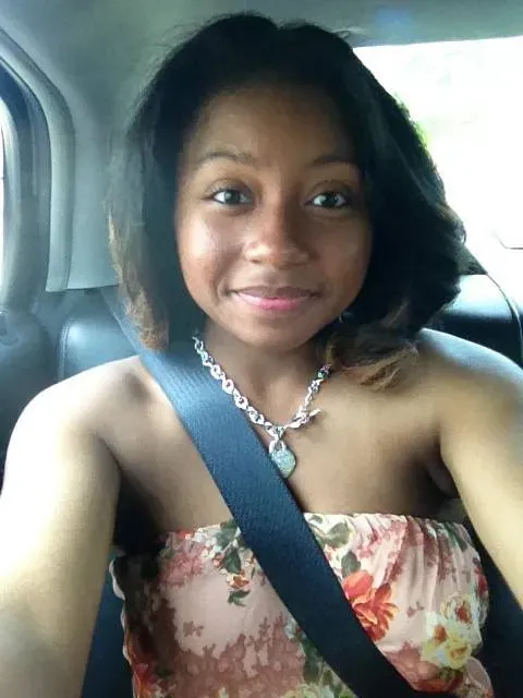 Woman smiling in a car, wearing a floral strapless top and seatbelt.