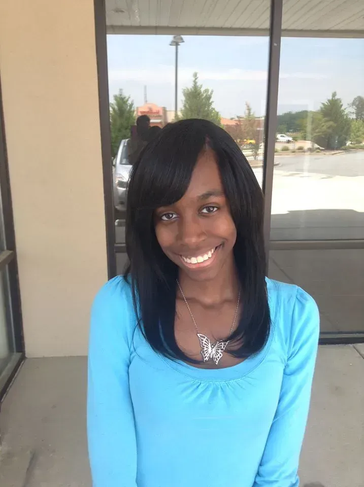Smiling person in a bright blue top standing outdoors by a glass-walled building