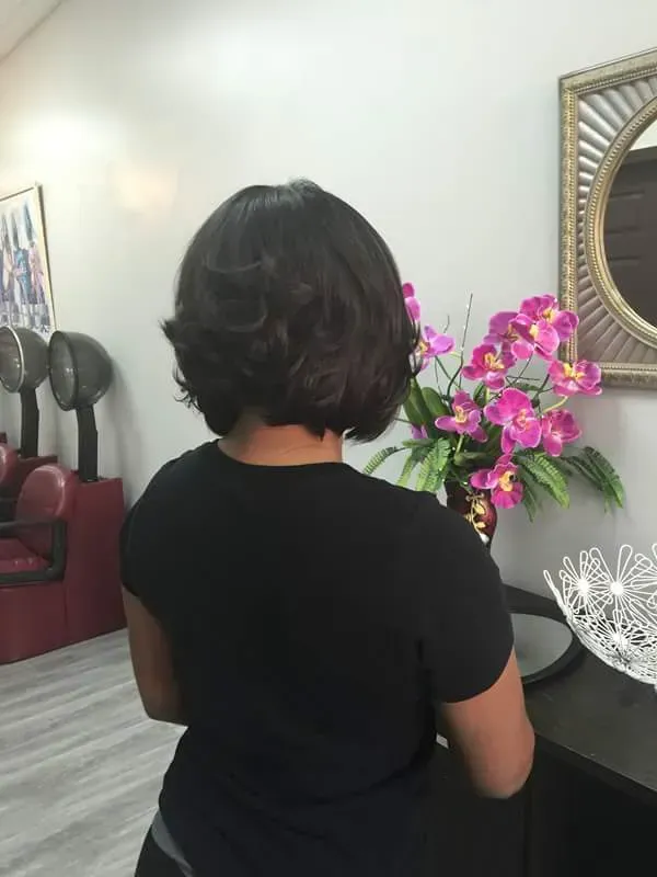 Person in black shirt standing by pink flowers in a living room, viewed from behind.