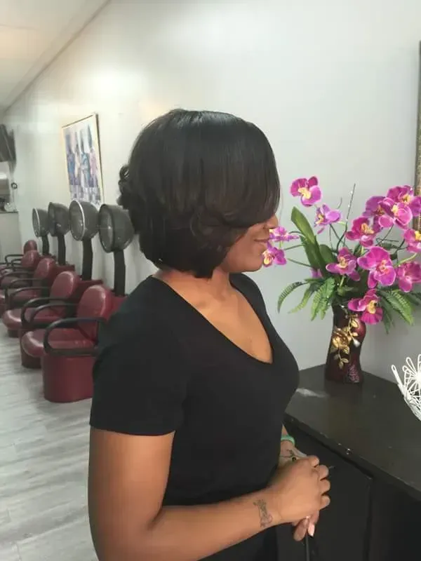 Woman in black top standing beside a desk with a pink flower arrangement in a salon waiting area