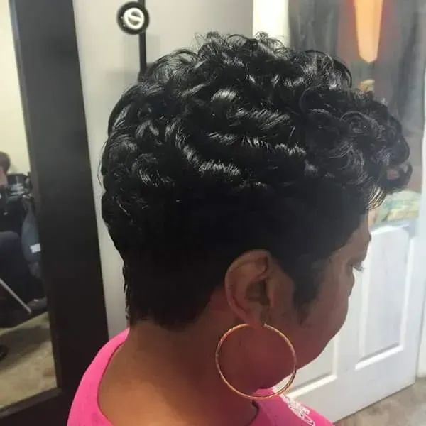Side view of a person with short curly black hair and a large gold hoop earring, indoors.