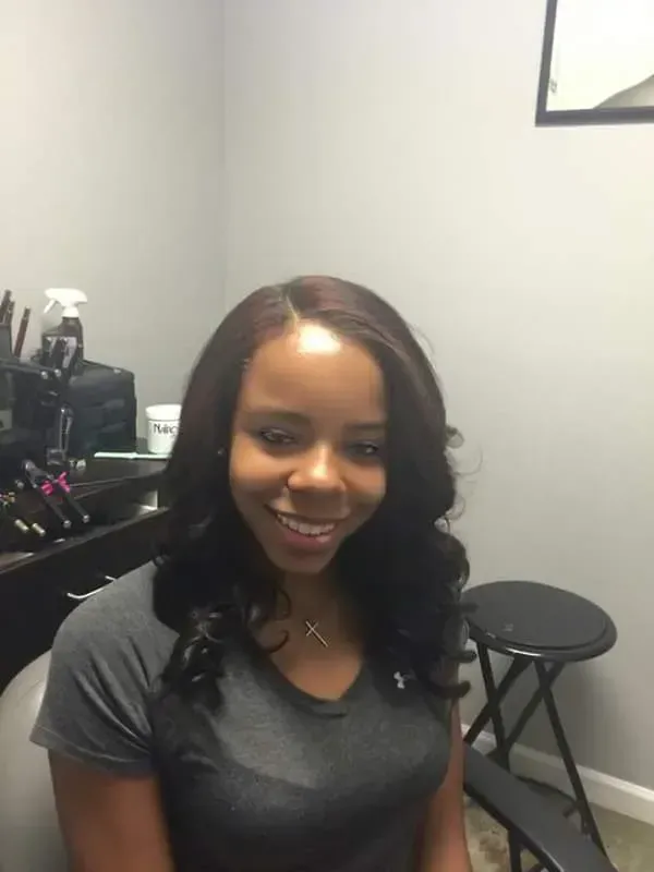 Smiling person seated in a salon chair beside styling tools and a stool.