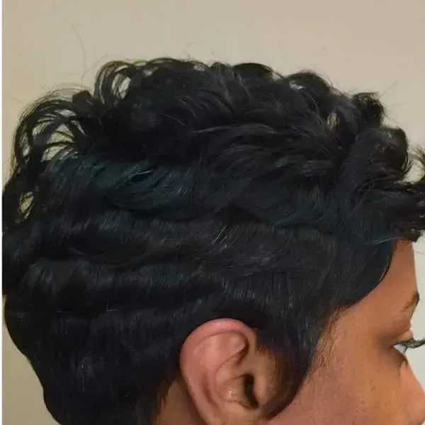 Side profile of a person with short, wavy black hair against a plain background
