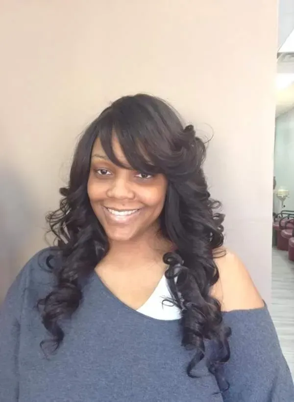 Smiling woman with long curly black hair wearing a dark gray off-shoulder top indoors