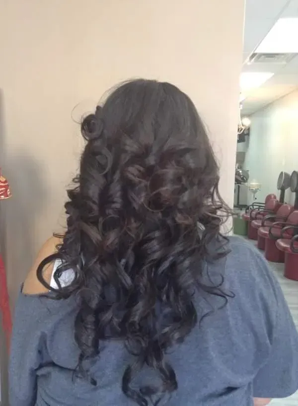 Back view of long, dark curly hair styled in loose curls, indoors near a hallway.